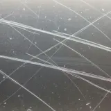 Gros plan sur une vitre très rayée, montrant des lignes fines et des éclaboussures d'eau. Idéal pour illustrer comment réparer une vitre rayée.