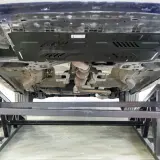 Vue du dessous d'une voiture sur des chandelles. Le système d'échappement est visible, ainsi qu'une plaque de protection. On dirait qu'il y a eu un choc sous la voiture.