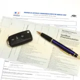 Carte grise, clé de voiture et stylo sur un document officiel.
