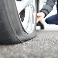 Un pneu qui se dégonfle sans crevaison, une personne accroupie examine la roue à plat.