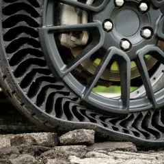 Gros plan sur une roue de voiture avec un pneu increvable, composé de multiples alvéoles noires, posé sur un sol dégradé.