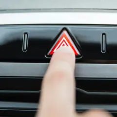 Un doigt appuie sur le bouton des feux de détresse, un triangle rouge lumineux sur le tableau de bord d'une voiture.
