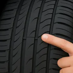 Un doigt pointe le témoin d'usure d'un pneu, indiquant qu'il est temps de le changer pour garantir la sécurité.