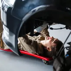 Mécanicienne travaillant sous une voiture, utilisant un chariot pour accéder à une pièce de réemploi.