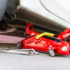 Un cric rouge est utilisé pour soulever une voiture. Des clés sont posées au sol, prêtes à être utilisées pour changer une roue.