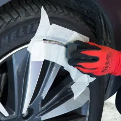Main d'une personne portant un gant rouge et noir, utilisant un produit pour réparer jante alu.