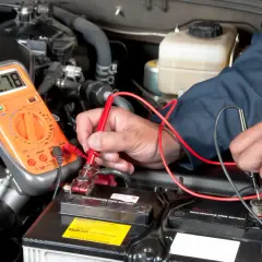 Un mécanicien vérifie la tension de la batterie d'une Mini Cooper. L'emplacement de la batterie est sous le capot, accessible pour le diagnostic.