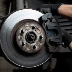 Main d'un mécanicien inspectant un disque de frein usé, une question se pose : quelle plaquette de frein choisir pour un freinage optimal ?