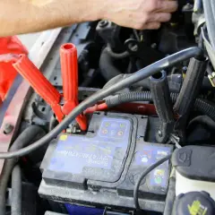 Comment brancher un booster de batterie : les pinces rouges et noires sont connectées à la batterie d'une voiture.
