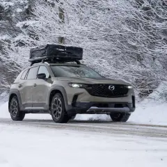 Un SUV gris roule sur une route enneigée, prêt à affronter l'hiver avec un coffre de toit chargé.