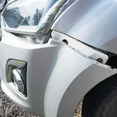 Le pare-chocs avant d'une voiture blanche est détaché, révélant une fissure carrosserie voiture. Le phare est visible.