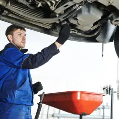 Mécanicien en bleu effectuant la vidange d'une voiture, prêt à changer l'huile. Savoir quand faire vidange voiture est essentiel.