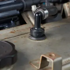 Détail d'un moteur de voiture, avec un tuyau noir fixé par un collier métallique. On aperçoit une pièce en caoutchouc noir, peut-être pour supprimer le reniflard d'huile.