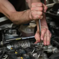Mécanicien utilisant un outil pour tenter de comment enlever un injecteur grippé sans extracteur. Gros plan sur les mains et le moteur.