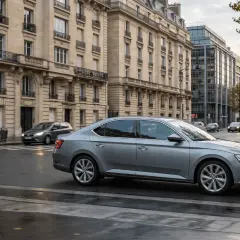 Une voiture grise circule dans une rue parisienne bordée d'immeubles haussmanniens. Une question se pose : c'est quoi ZFE ?