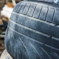 Gros plan sur un pneu lisse, usé par le temps et les kilomètres parcourus. Les sculptures sont à peine visibles, témoignant d'une longue vie sur la route.