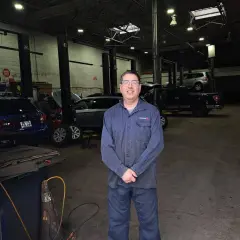 Homme souriant dans un garage libre service pour réparer soi-même. Plusieurs voitures sur des ponts élévateurs.