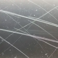 Gros plan sur une vitre très rayée, montrant des lignes fines et des éclaboussures d'eau. Idéal pour illustrer comment réparer une vitre rayée.