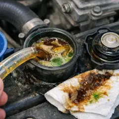 Une main verse un liquide brun dans le réservoir du liquide de refroidissement, où il se mélange à un liquide verdâtre, formant une émulsion d'huile dans liquide de refroidissement.