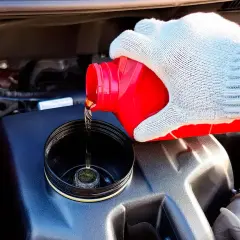 Maintenant, vous savez où se trouve le liquide de frein de votre Mini Cooper. Une main gantée verse le liquide d'un bidon rouge dans le réservoir.