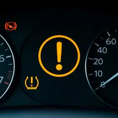 Tableau de bord d'une voiture avec voyant moteur point d'exclamation allumé, ainsi que des voyants de pression des pneus et de frein à main.