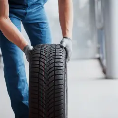 Un mécanicien en bleu tient un pneu d'hiver, une sous-marque Michelin, prêt pour le montage.