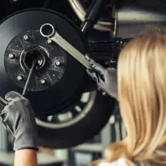 Mécanicienne travaillant sur un frein, vérifiant un piston frein bloqué avec une clé.