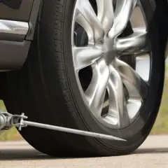 Cric de voiture soulevant un véhicule, avec une roue de secours à proximité.