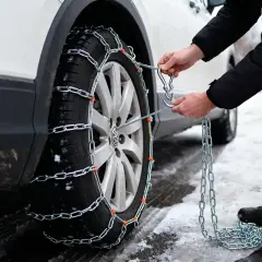 Comment mettre des chaînes neige : un homme attache une chaîne à un pneu de voiture sur une route enneigée.