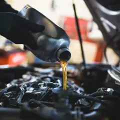 Main d'un mécanicien versant de l'huile neuve dans le moteur d'une Dacia Sandero lors d'une vidange.