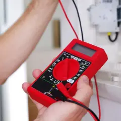 Main rouge pour tester un fusible voiture avec un multimètre.