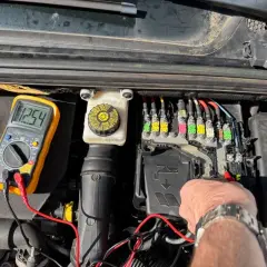 Diagnostic d'une C4 phase 2 : un multimètre affiche 12.54V près du boîtier de fusibles, indiquant une vérification avant de changer la batterie.
