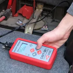 Utilisation d'un testeur de batterie avancé pour savoir comment tester une batterie sans multimètre. L'appareil affiche 12.14V.
