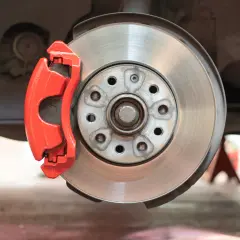 Gros plan sur un disque de frein usé, avec un étrier rouge vif.