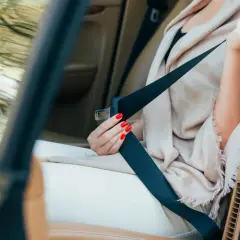 Main tenant, une femme aux ongles rouges s'apprête à changer ceinture de sécurité dans une voiture de luxe.