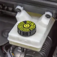 Réservoir de liquide de frein avec bouchon noir et jaune. Le niveau du liquide est visible, indiquant la nécessité d'un contrôle du liquide de frein.