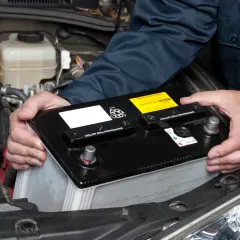 Un mécanicien installe une nouvelle batterie de voiture. Le poids de la batterie est géré avec soin.
