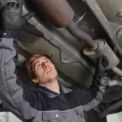 Mécanicien inspectant le pot catalytique d'une voiture, sous le véhicule.