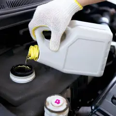 Main d'un mécanicien en gant blanc versant du liquide de frein neuf dans le réservoir. Le prix du changement de liquide de frein est un entretien essentiel.