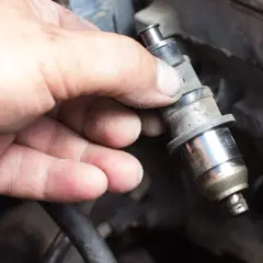 Main d'un mécanicien tenant un injecteur diesel sale, prêt à nettoyer injecteur diesel soi-même.