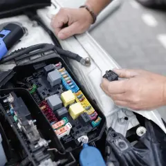 Un mécanicien examine le boîtier de fusibles d'une voiture, cherchant la cause d'un problème électrique. Il tient un relais dans sa main.