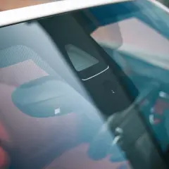 Vue rapprochée du pare-brise d'une voiture, montrant un capteur de luminosité et d'autres éléments électroniques.