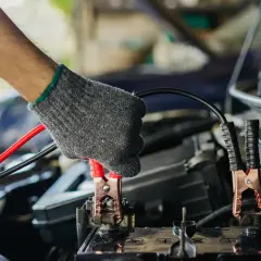 Main tenant un câble pour démarrer une voiture. La pince rouge est connectée à la batterie.