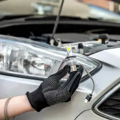 Main tenant une ampoule LED neuve, prêt à changer les ampoules de phare d'une voiture argentée.