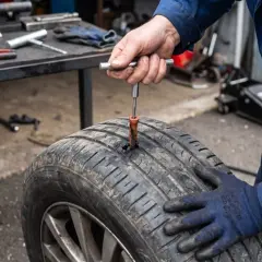 Un mécanicien utilise un outil pour insérer une mèche dans un pneu crevé, prêt à réparer la crevaison.