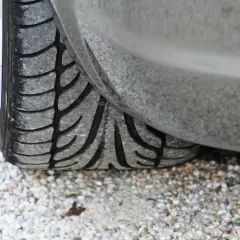 Gros plan sur un pneu de voiture usé, posé sur des graviers. J'espère que mes pneus font du bruit quand je roule, car ils sont en fin de vie !