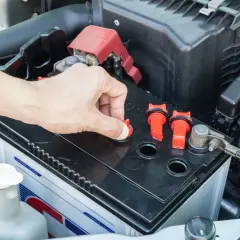 Main d'une personne ouvrant un bouchon sur une batterie de voiture, peut-être pour vérifier le niveau d'eau pour batterie.