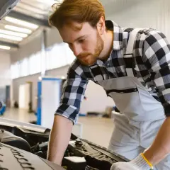 Mécanicien concentré sur le moteur d'une voiture, prêt à effectuer une vidange. Il se demande combien de litre d'huile pour une vidange.