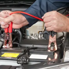 Mains de mécanicien connectant des câbles de démarrage à une batterie de voiture. On peut charger une batterie sans la débrancher.