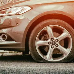 Gros plan sur une roue de voiture Ford avec un pneu crevé, le flanc complètement à plat sur l'asphalte. Une vraie galère !